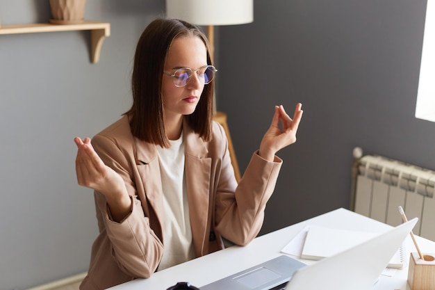 Portrait of calm young adult young businesswoman working online\
on notebook in home office and having break trying to calm down\
practicing yoga at workplace