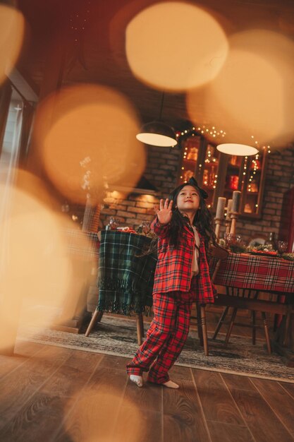 Photo portrait of candid asian smiling little girl in red plaid pajama joy emotion at wooden lodge xmas