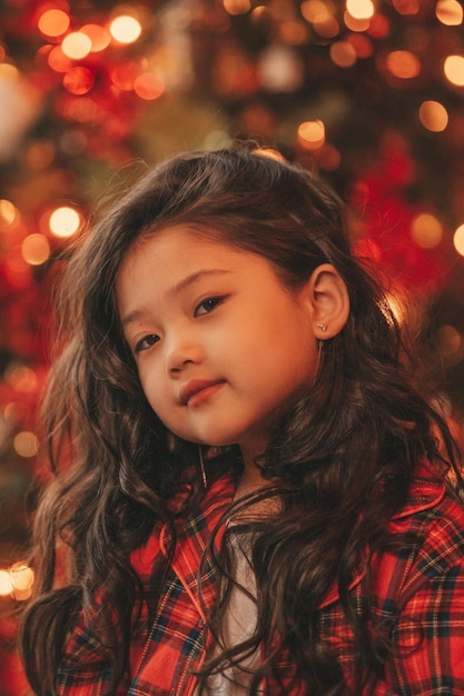 Portrait of candid authentic asian dreamer little girl in red plaid pajama waiting Santa at Xmas