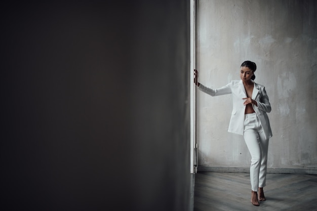率直な本物のエレガントなセクシーな混血モデルの女の子の肖像画は、ブラと白いパンツ スーツでポーズをとる