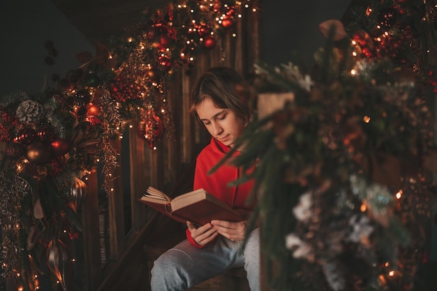 Portrait of candid authentic smiling boy teenager reading book on distance studying at home xmas