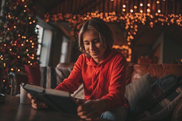 Portrait of candid authentic smiling boy teenager reading book on distance studying at home Xmas