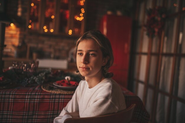 Photo portrait of candid authentic smiling handsome boy teenager using mobile phone at xmas home interior