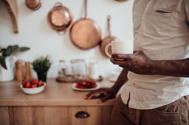 Портрет откровенного красивого темнокожего мужчины делает перерыв на кофе и отдыхает на уютной деревенской кухне