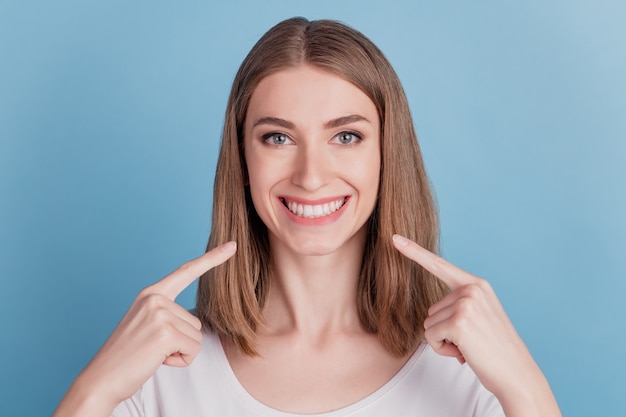 Il ritratto della ragazza sana candida indica il sorriso a trentadue denti dell'indice su fondo blu