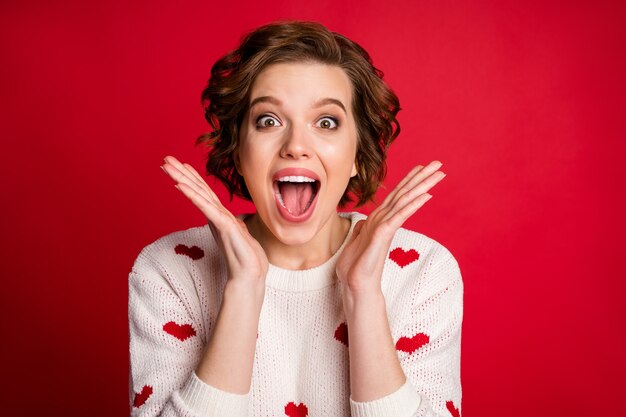 Il ritratto delle mani incrociate dell'amante della ragazza carina adorabile candida indossa il maglione alla moda elegante isolato sulla parete rossa