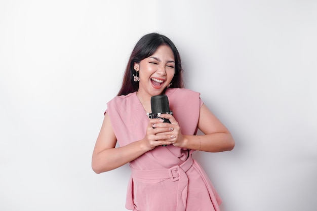 Portrait of carefree Asian woman having fun karaoke singing in microphone while standing over white background
