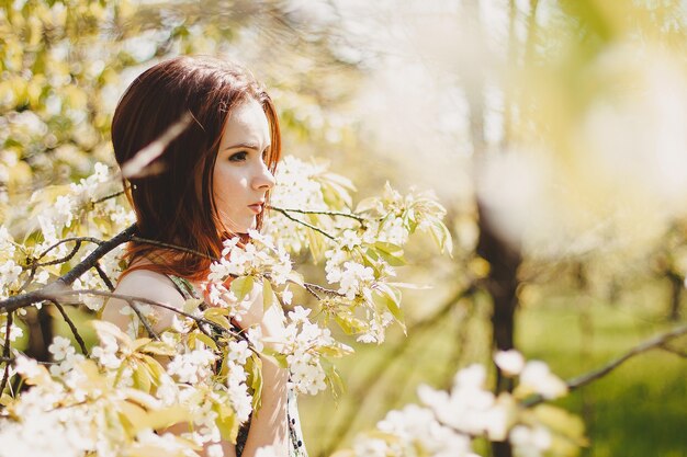 Portrait of carefree young woman in boho style dress in spring cherry blossom garden.