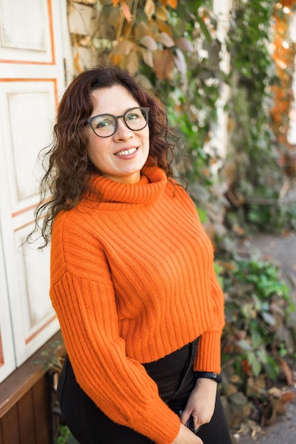 Портрет беззаботной молодой женщины, улыбающейся на городском фоне, веселой латинской девушки в очках