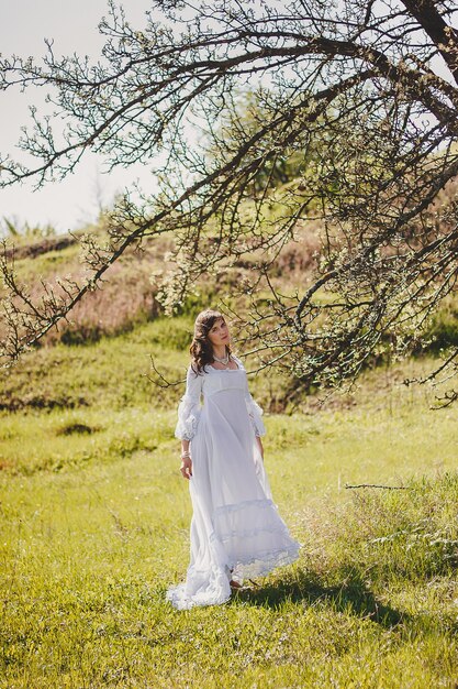 Portrait of carefree young woman in white vintage wedding style dress in spring garden valley