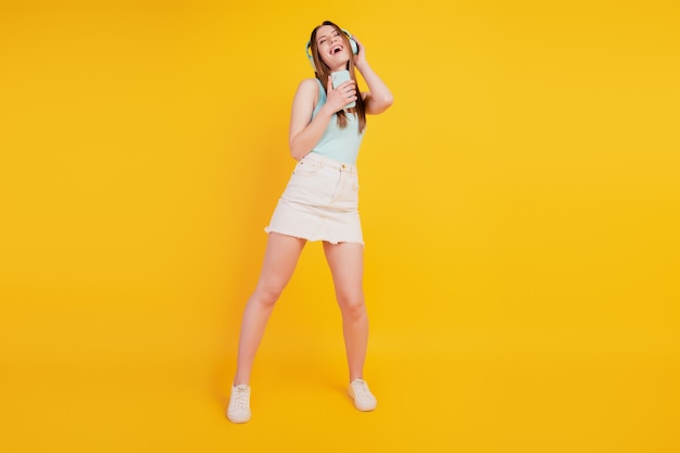 Portrait of careless singer pretty lady dance sing song listen music on yellow background