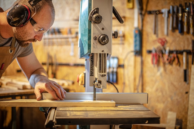 Portrait of a carpenter inside his carpentry workshop using a band saw.