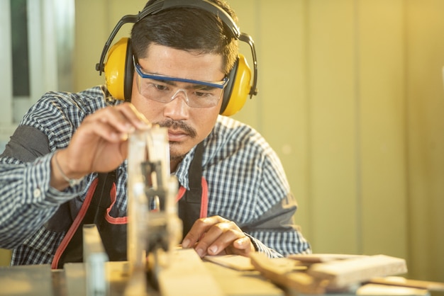 写真 肖像画の大工の男幸せな魅力的な勤勉な探してワークショップで木材を選択します。大工は大工店の木製のテーブルの機器を操作します。