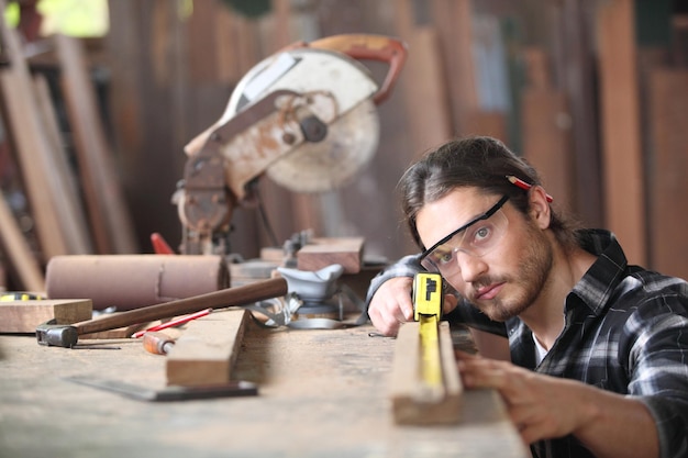 Photo portrait of carpenter measuring wooden plank in workshop