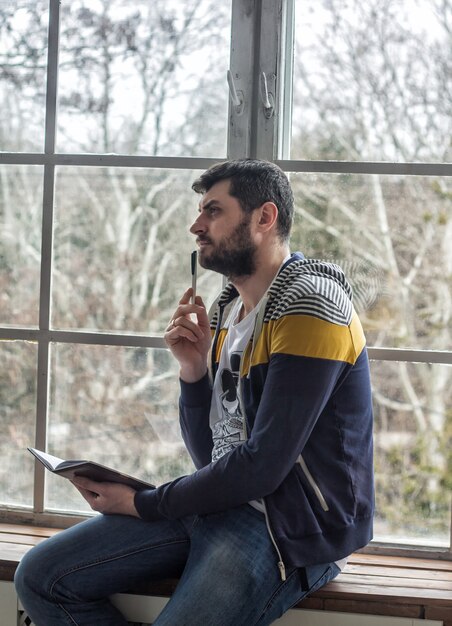 Portrait of a casual bearded hipster man thinking  holding pen and making notes in copybook