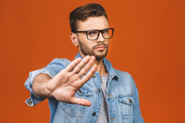 Portrait of a casual man showing stop sign isolated over orange background.