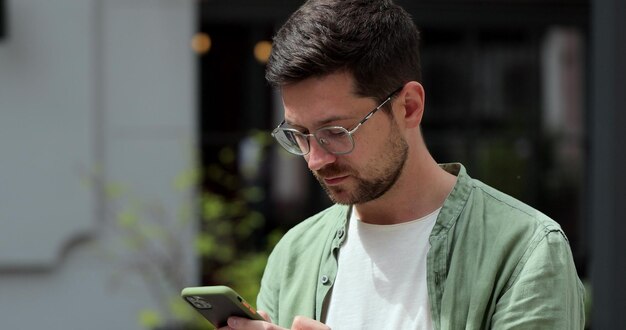 Foto ritratto di uomo casual che utilizza lo smartphone all'aperto uomo allegro che digita messaggi sul telefono all'esterno messaggistica online e navigazione in internet