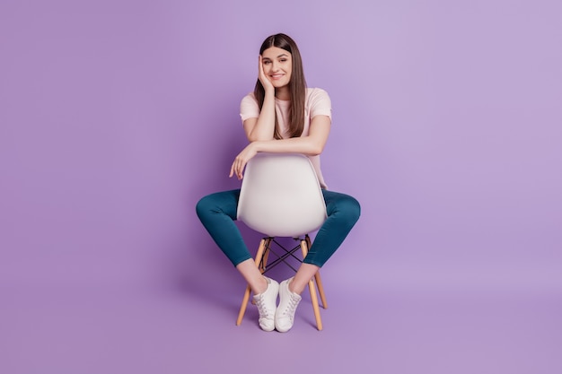 Portrait of casual trendy adorable lady sit chair palm cheekbone look camera on purple background