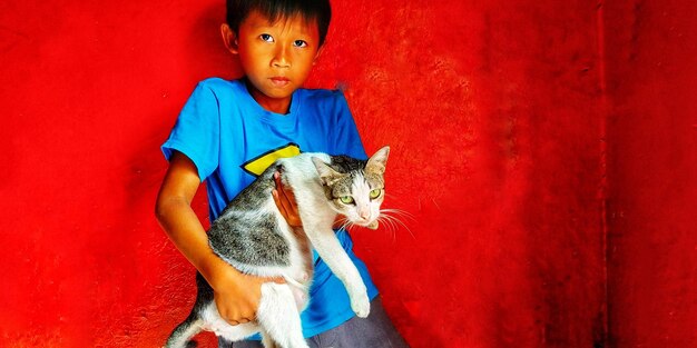 Portrait of cat sitting on red wall