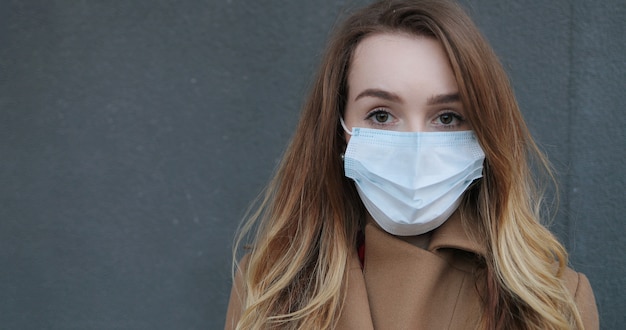 Portrait of Caucasian beautiful woman in medical mask standing outside. Pandemic concept, coronavirus epidemic.