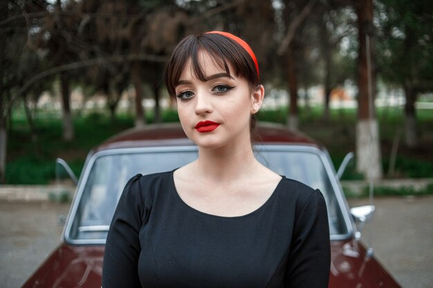 Portrait of a Caucasian beautiful young girl in a black vintage dress, posing near a vintage car 