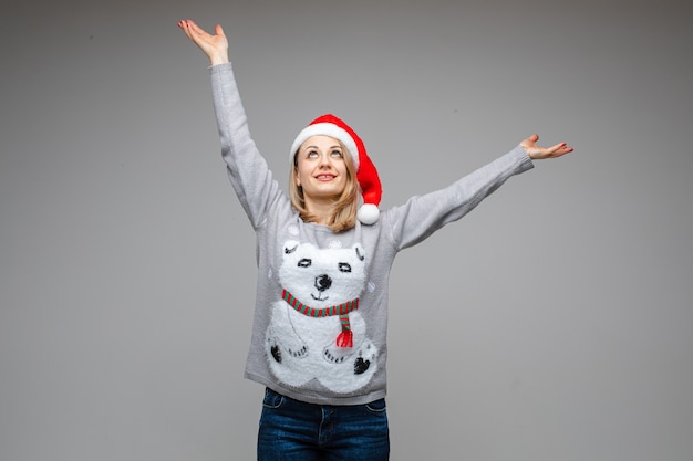 Portrait of Caucasian blonde woman in red Santa hat and winter sweater with polar bear outstretching her arms