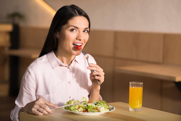 Portrait of caucasian businesswoman eating fresh salad in cafe and looking at camera