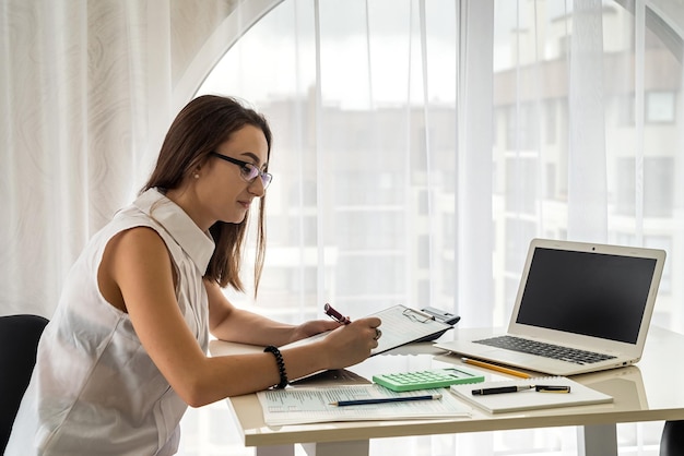 안경을 쓴 백인 여성 사업가의 초상화는 사무실에서 노트북을 사용한다