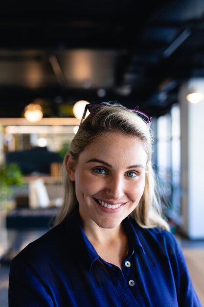 Portrait of a Caucasian businesswoman with blond hair, wearing navy blue shirt, working in modern office, smiling and looking straight into a camera.