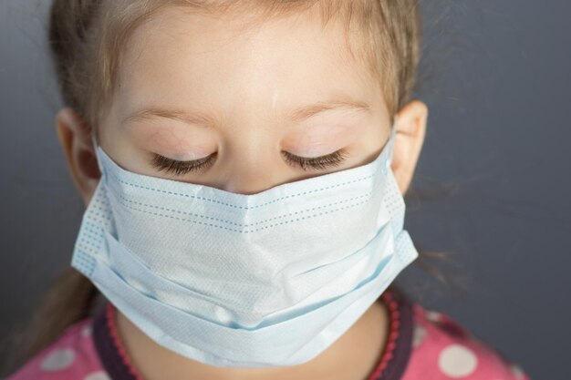 Portrait of caucasian child of three years old with mask on face looking down on the gray background