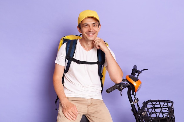 Portrait of Caucasian courier man of takeaway food on electric scooter looking at camera waiting orders expressing happiness fast delivery posing isolated over purple background