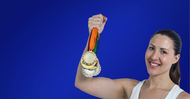 Portrait of caucasian female athlete holding multiple medals smiling against blue background