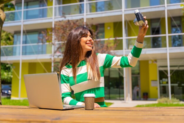 Portrait of a caucasian girl working with a computer in nature taking a selfie with a vintage camera