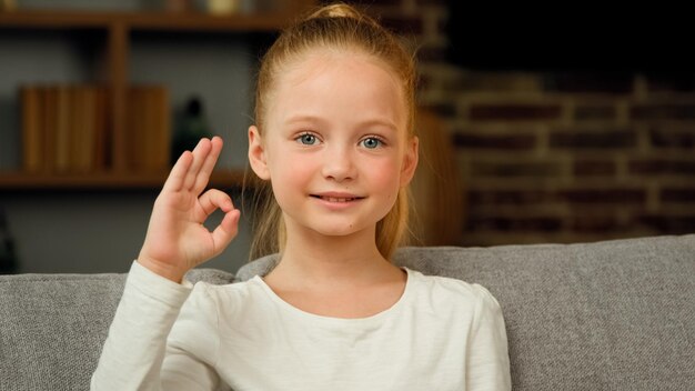 Ok のジェスチャーを示すカメラを見て笑顔の子供の白人の幸せな子供の女の子の肖像画をお勧めします