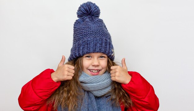 Portrait of caucasian happy smiling little girl in red down jacket with blue hat and scarf of years