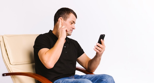 Portrait of a caucasian hearing impaired man sitting in a chair, holding hand on his ear