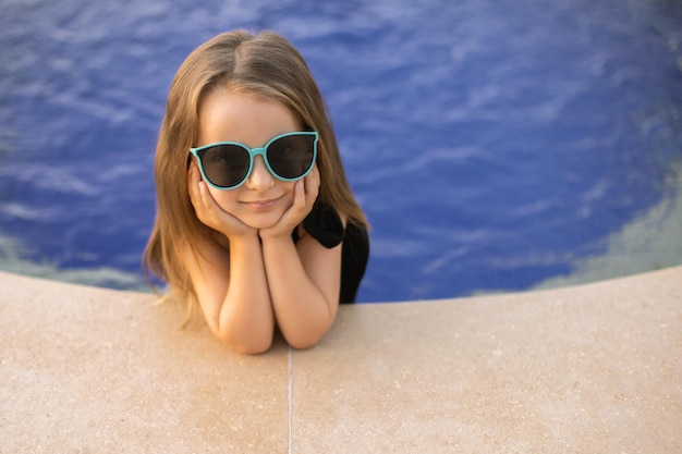 Portrait of caucasian little girl put her hands on the edge of the pool and her feet in the water