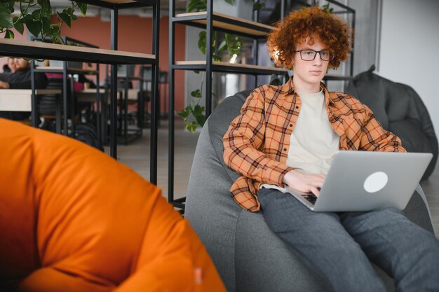 Portrait of Caucasian male freelancer in trendy apparel sitting at cafeteria table and doing remote work for programming design of public website skilled software developer posing in coworking space