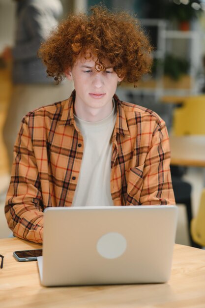 Portrait of Caucasian male freelancer in trendy apparel sitting at cafeteria table and doing remote work for programming design of public website skilled software developer posing in coworking space