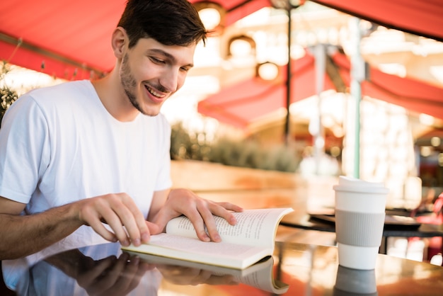 自由な時間を楽しんで、コーヒーショップで屋外に座って本を読んでいる白人男性の肖像画。ライフスタイルのコンセプト。