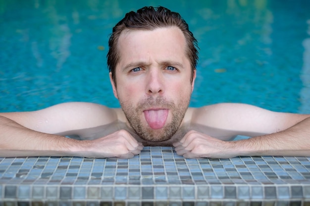 Portrait of a caucasian man putting out his tongue resting in the swimming pool