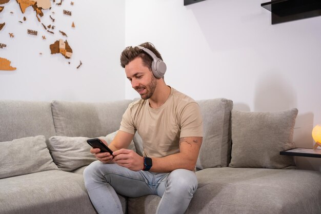 ソファに座って携帯電話とヘッドフォンを使用する白人男性のポートレート