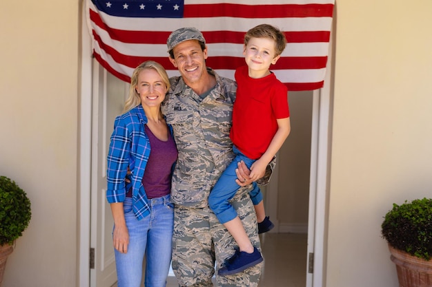 Portrait of caucasian military man with woman and carrying son standing at house entrance. family, love and patriotism concept, unaltered