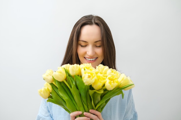 Portrait of caucasian smiling brunette woman with yellow tulips with closed eyes