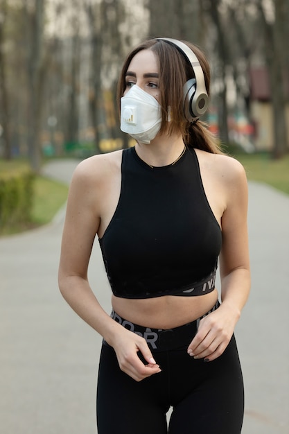 Портрет кавказской sporty женщины нося лицевой щиток гермошлема медицинской защиты пока бегущ в парке. Вирус короны или Covid-19 распространяется по всему миру.
