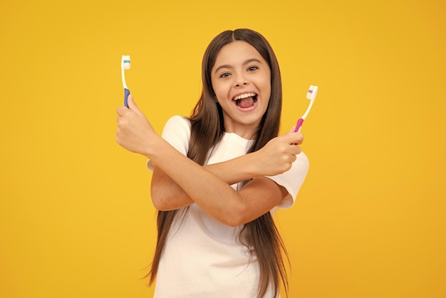 Портрет кавказской девочки-подростка держит зубную щетку, чистя зубы утренней гигиеной зубов, изолированной на желтом фоне