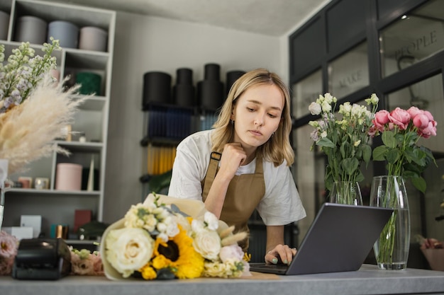 Portrait of Caucasian woman entrepreneur sitting in own flower shop typing on laptop