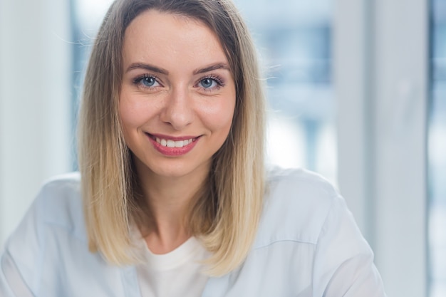 portrait a caucasian young blonde woman indoors looking at camera and smiling