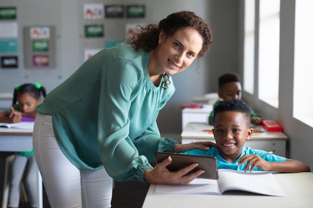 Photo portrait of caucasian young female teacher with african american elementary schoolboy at desk