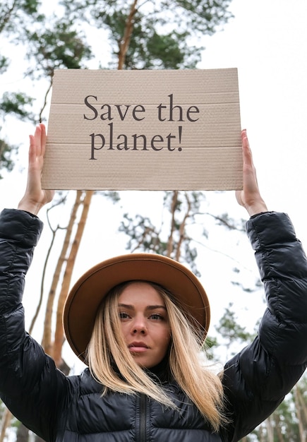 Photo portrait of caucasian young woman in hat holding cardboard with text outdoors nature background